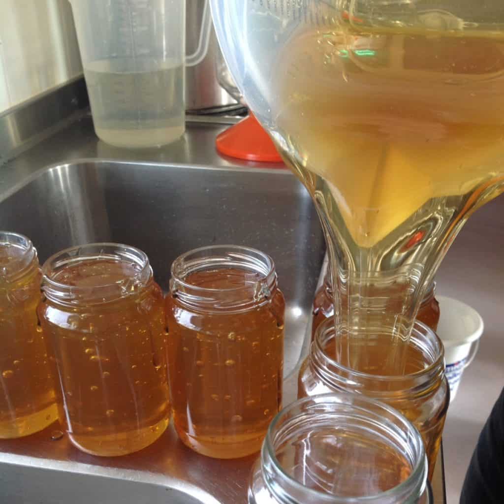 Honing wordt uit een kan in honingpotjes gegoten